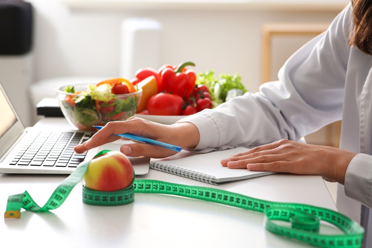 A woman planning a healthy diet in front of a computer surrounded by different fruits and vegetables