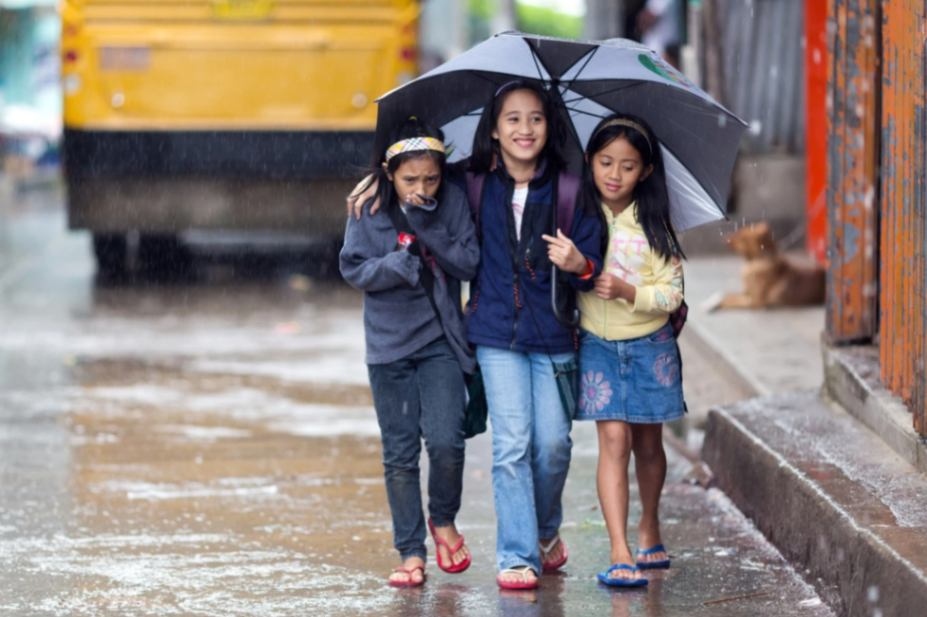 a group of children in the Philippines sharing one umbrella under the rain to keep safe and prevent asthma attack